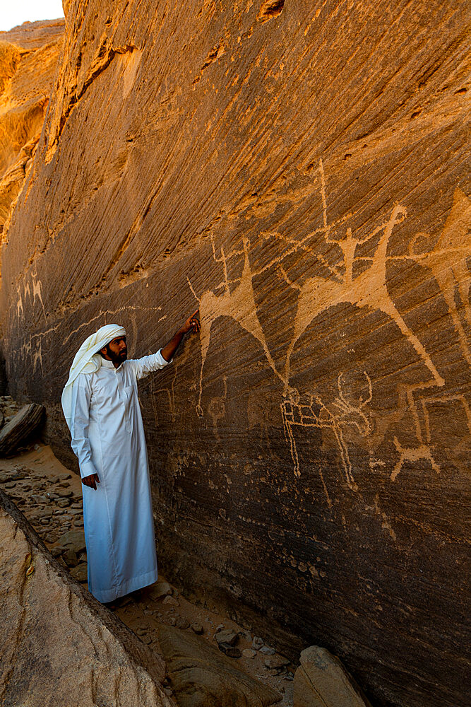 Man pointing at rock carvings, Bir Hima Rock Petroglyphs and Inscriptions, UNESCO World Heritage Site, Najran, Kingdom of Saudi Arabia, Middle East