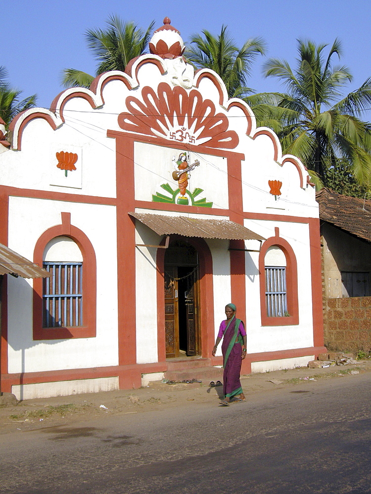 India. Woman walking past a hindu temple in goa.