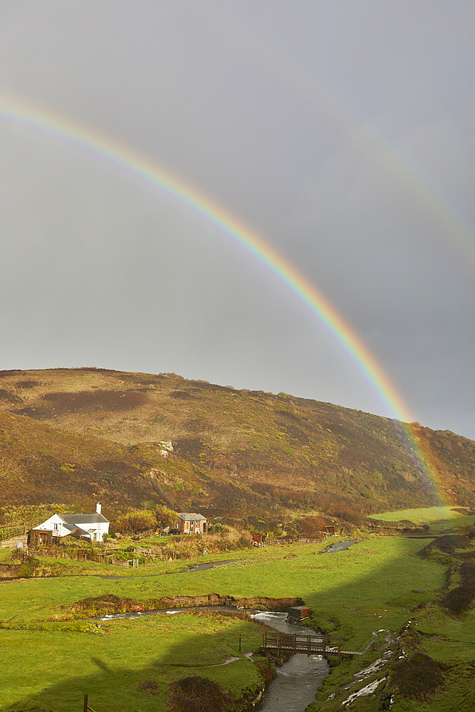 A valley rainbow forms in the face of an autumn squall, in Duckpool, a remote cove near Bude, north coast of Cornwall, England, United Kingdom, Europe