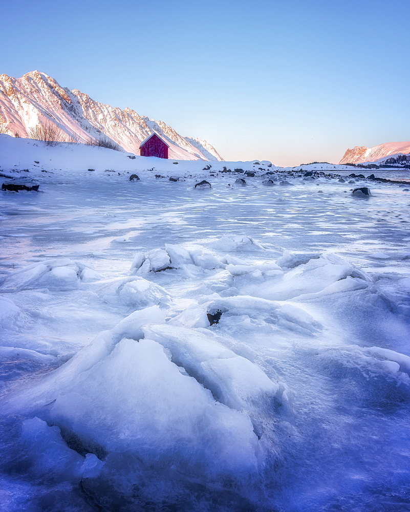 Red rorbuer hut set against a frozen lake, Lofoten Islands, Nordland, Norway, Europe