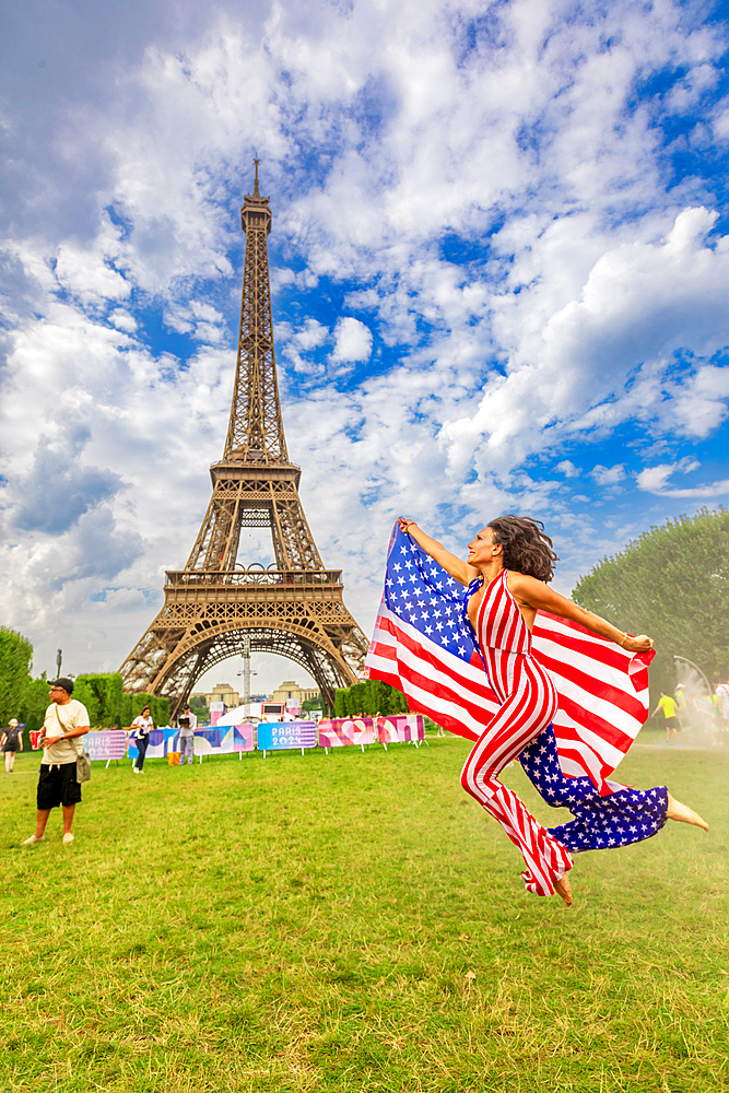 Patriotic American Woman jumping and cheering for Team USA and the Paris 2024 Olympics in front of the Eiffel Tower, Paris, France, Europe