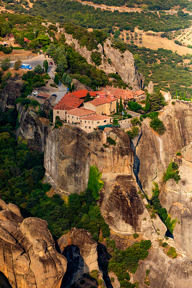 Aerial view in vertical orientation of a Meteora monastery perched on a high rock formation, surrounded by dramatic cliffs and greenery, Thessaly, Greece.