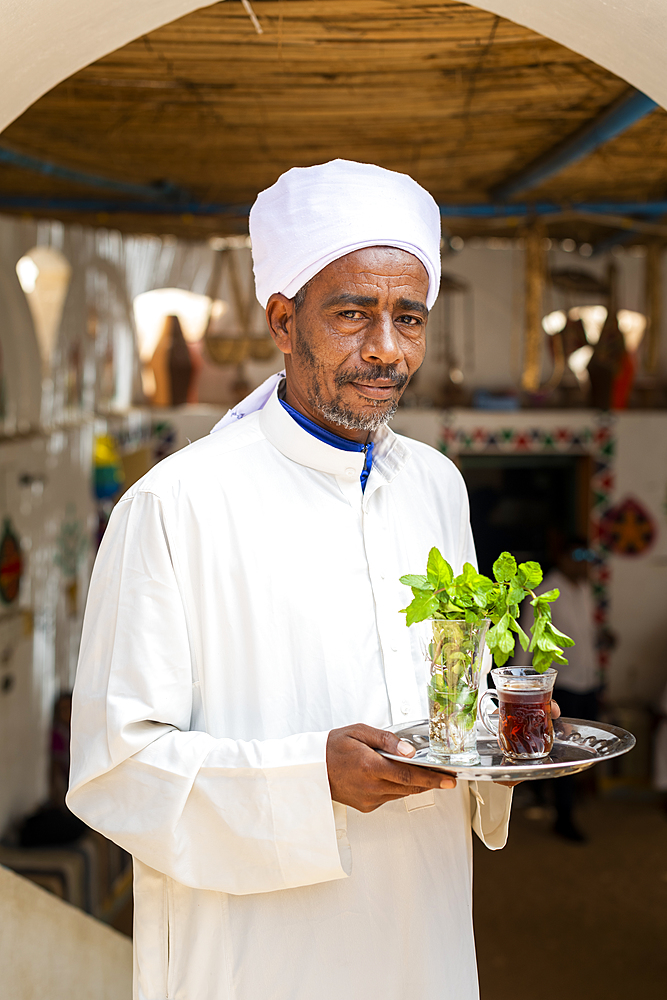 An Egyptian man holds a tray with a glass of mint tea and some fresh mint leaves, Aswan, Egypt, North Africa, Africa