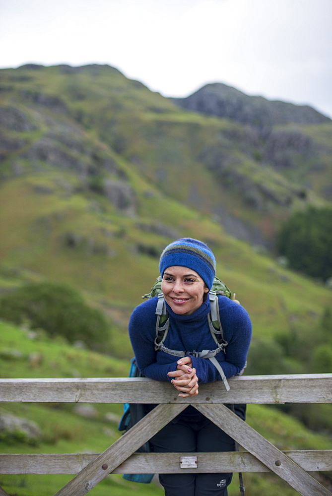 A woman rests on a gate in the Great Langdale valley in The Lake District, Cumbria, England, United Kingdom, Europe