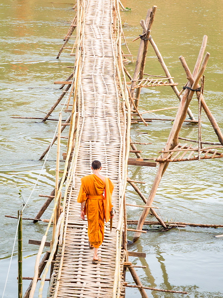 Orange-clad Buddhist monk crossing a bamboo bridge, Luang Prabang, Laos, Indochina, Southeast Asia, Asia