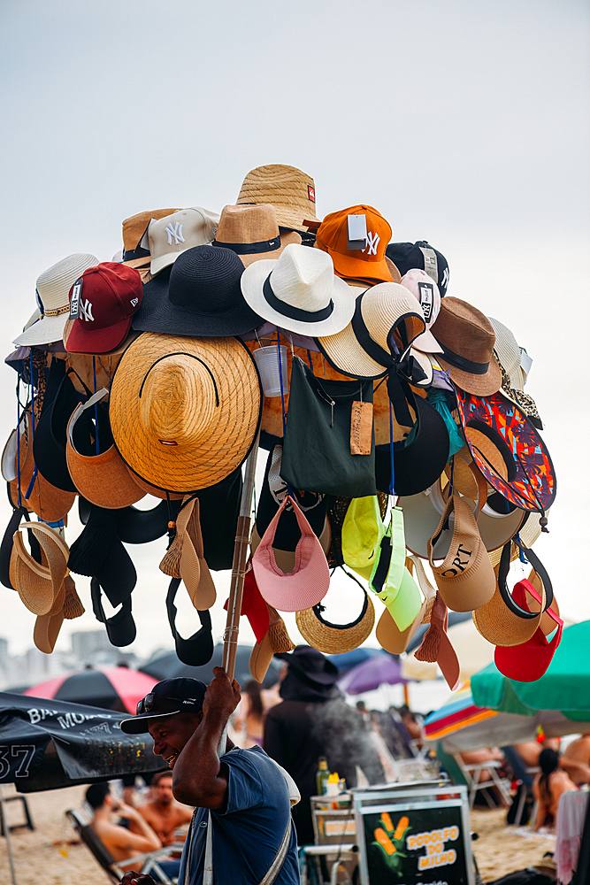 Salesman displaying hats for sale, at Leblon beach in Rio de Janeiro, Brazil, South America