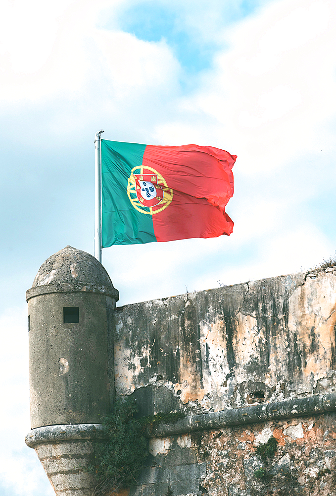 A weathered stone fort and Portuguese flag flying from flagpole on a small turret, Lisbon, Portugal, Europe