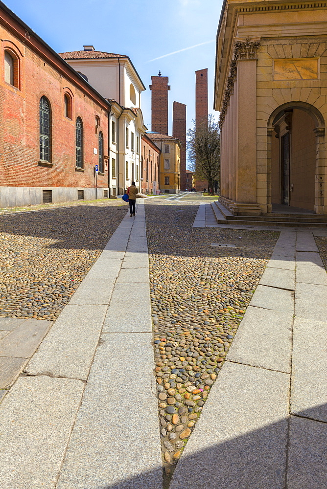 One person walks in a street with medieval towers in the background, Pavia, Pavia province, Lombardy, Italy, Europe