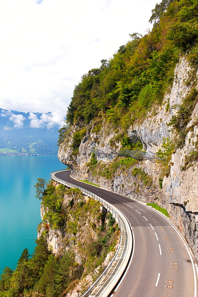 A curved road built into the side of a mountain next to Lake Thun, Interlaken, Bernese Oberland, Bern, Switzerland, Europe