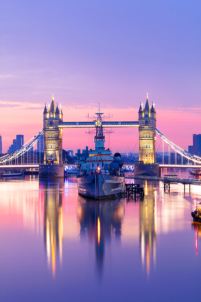 Sunrise view of HMS Belfast and Tower Bridge reflected in River Thames, with Canary Wharf in background, London, England, United Kingdom, Europe