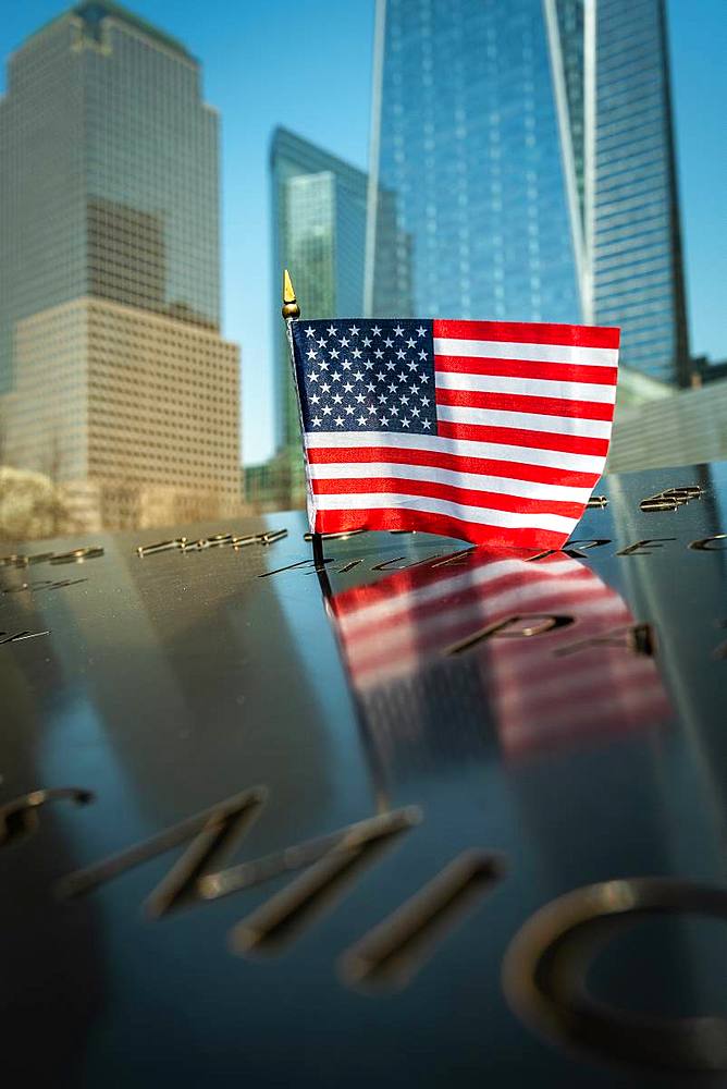 A small American flag at the 9/11 Memorial Park in New York City with the new World Trade Centre rising in the background, New York, United States of America, North America