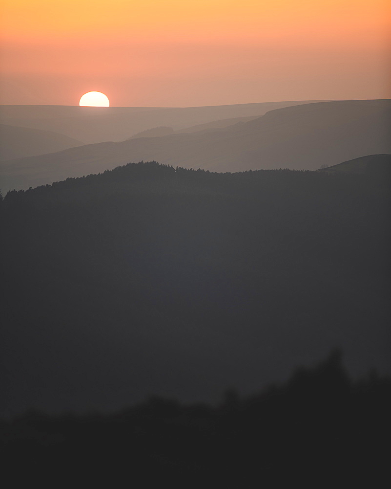 A beautiful sunset with the sun just dipping behind the hills in the Peak District National Park, Derbyshire, England, United Kingdom, Europe