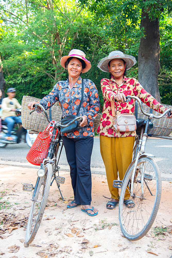 Two local women with their bicycles smiling together in Siem Reap, Cambodia, Indochina, Southeast Asia, Asia