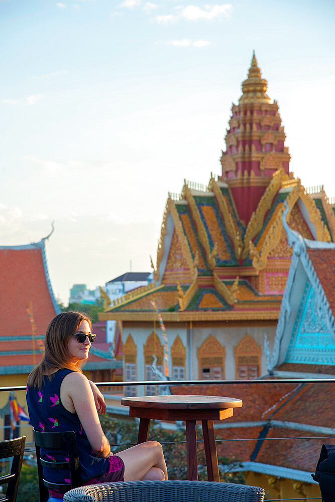 A female tourist sitting at a rooftop restaurant overlooking a temple in Phnom Penh, Cambodia, Indochina, Southeast Asia, Asia