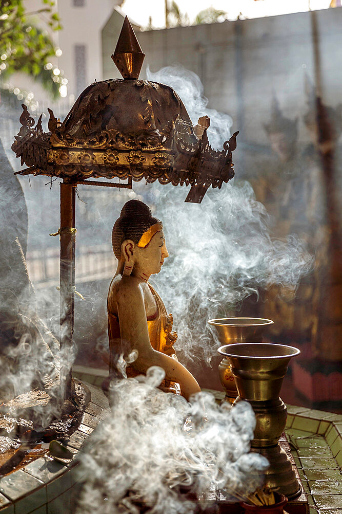 A small Buddha statue at Sule pagoda, surrounded by clouds of smoke with two Kinaree statues visible in the background, Yangon (Rangoon), Myanmar (Burma), Asia