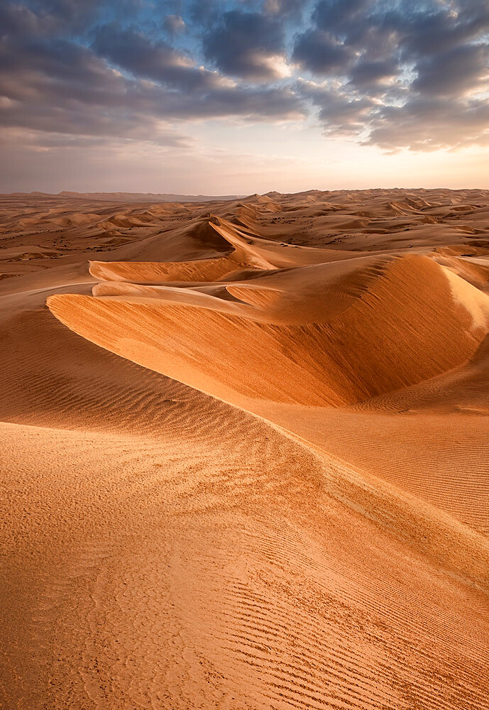 Sand dunes at sunset in the Wahiba Sands desert with clouds in the sky, Oman, Middle East