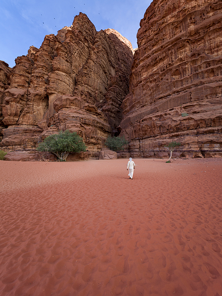 A beduin with traditional white clothes walking towards a canyon in Wadi Rum desert in Jordan