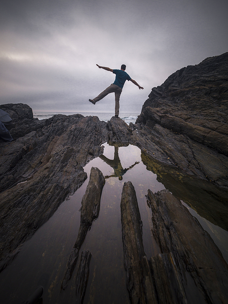 A man balancing on one leg on the rocks and his reflection in a pond of water, Spain, Europe