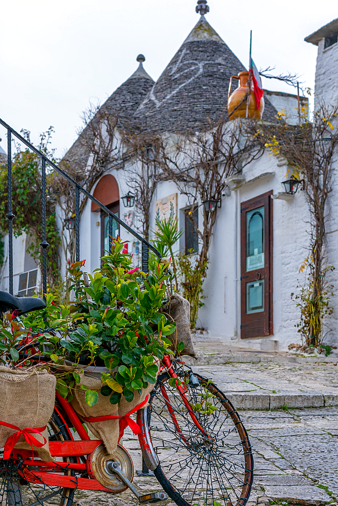 Red bike with flowers near a iconic Trullo house with conic ceiling in Alberobello, Italy