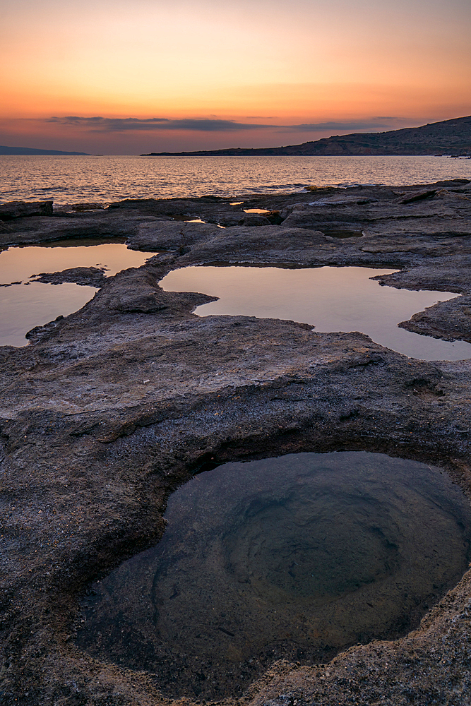 Natural holes on the rocks full with water at sunset with turquoise water sea of Greece on the background