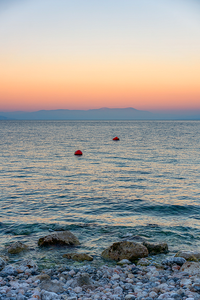 Wild pebble beach in Greece at sunset with turquoise water and mountains in the background