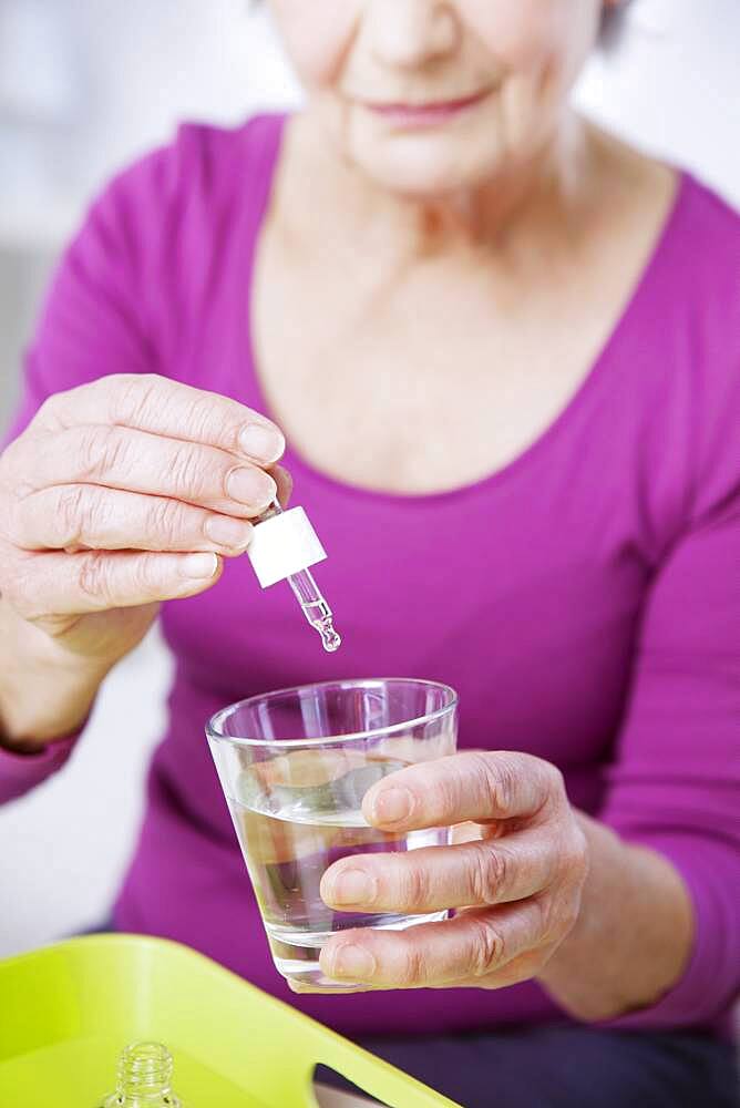 Senior woman pouring essential oil in a glass of water.