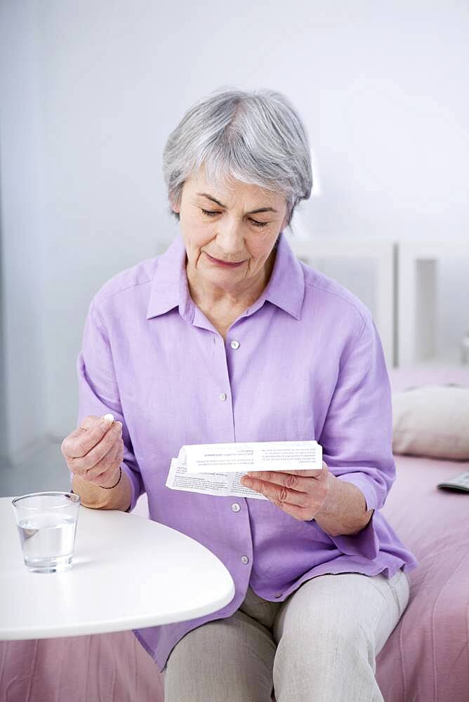 Senior woman reading medication instruction sheet.