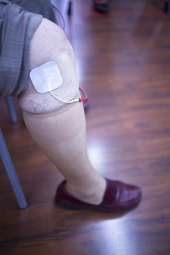 Female patient knee, leg, thigh and calf in physiotherapy rehabiliation treatment from injury in hospital clinic with electrical stimulus attached with plaster.