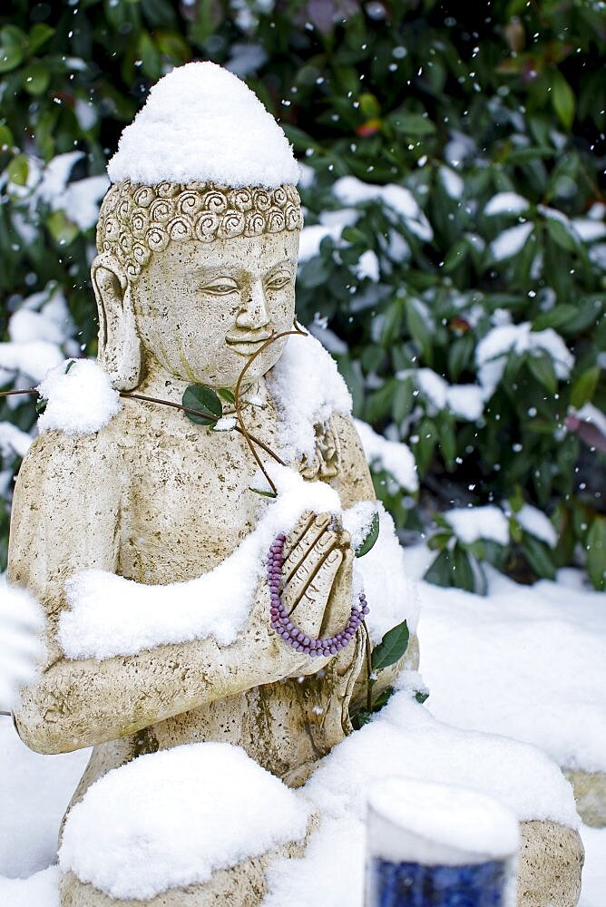 Buddha stony statue under the snow in winter season in a garden.