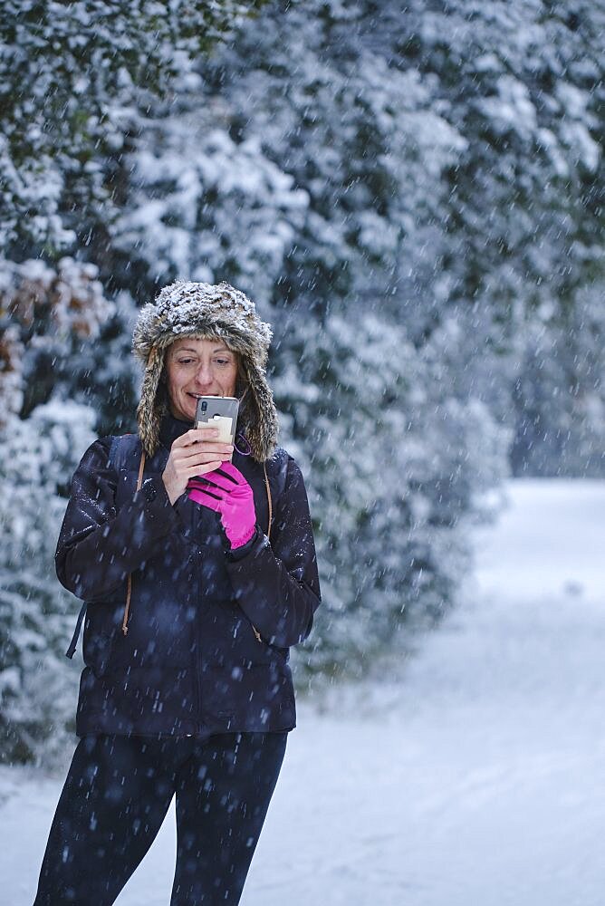 Caucasian young woman enjoying with a mobile phone in snow outdoor in winter time. Navarre, Spain, Europe.