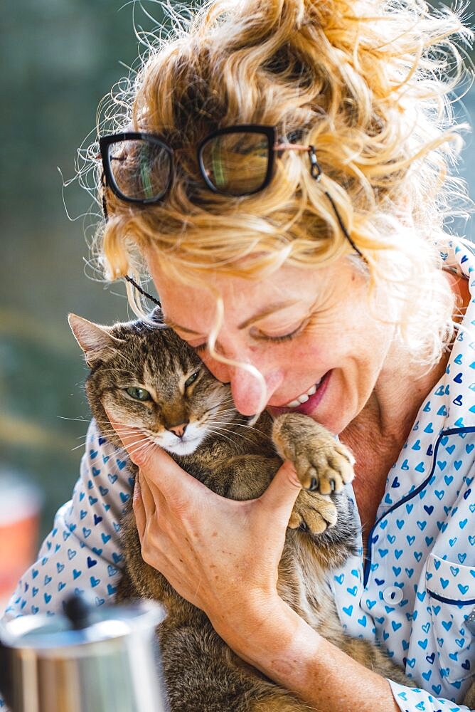 Blonde young mature woman with glasses in pijamas at home in breakfast time, reading a magazine and having a moment with her cat.