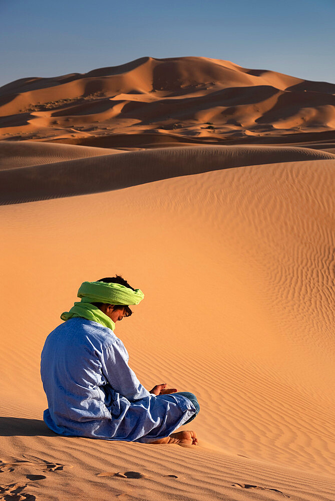 A Berber man in traditional dress sits amongst the Sand Dunes of Erg Chebbi, Sahara Desert, Morocco, North Africa, Africa