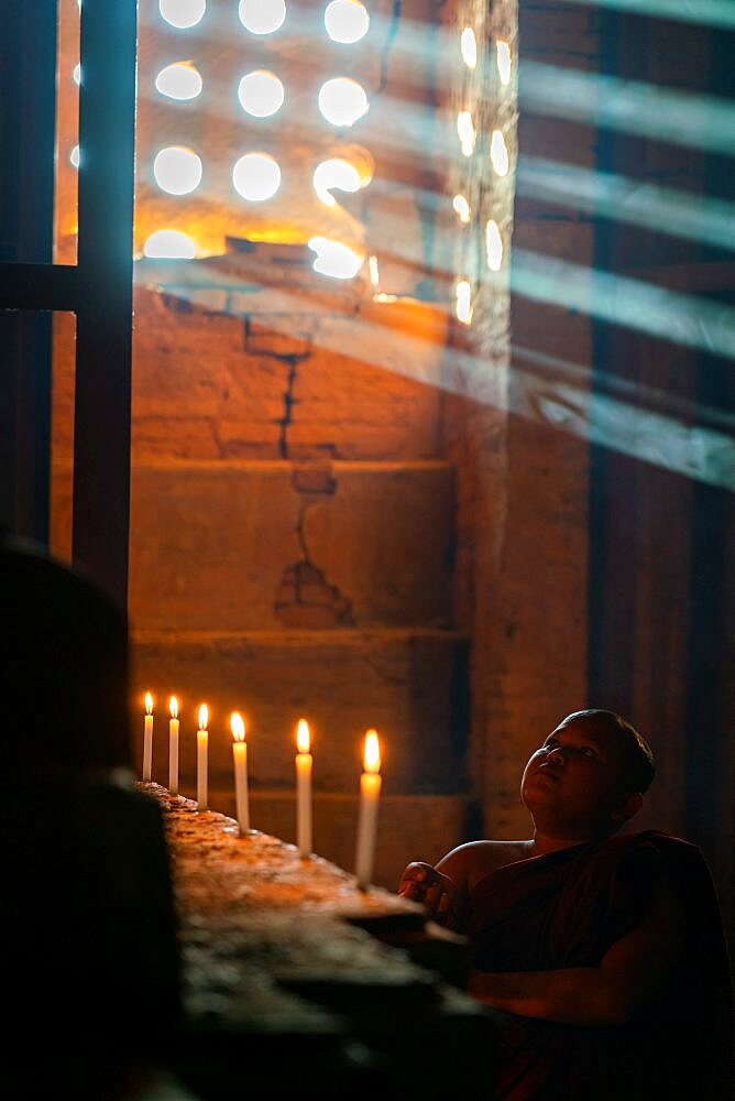 Novice monk inside temple looking up to Buddhist statue, UNESCO, Bagan, Myanmar