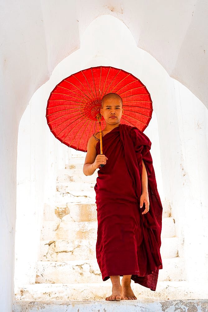 Novice monk with umbrella standing at staircase hallway at Hsinbyume pagoda, Mingun, Mandalay, Myanmar