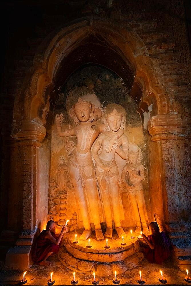 Two novice monks holding candles at statue inside temple, Bagan, Myanmar