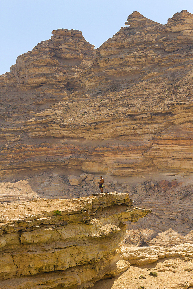 Man standing on cliff against mountains, Wadi Sinaq, Dhofar Governorate, Oman, Middle East