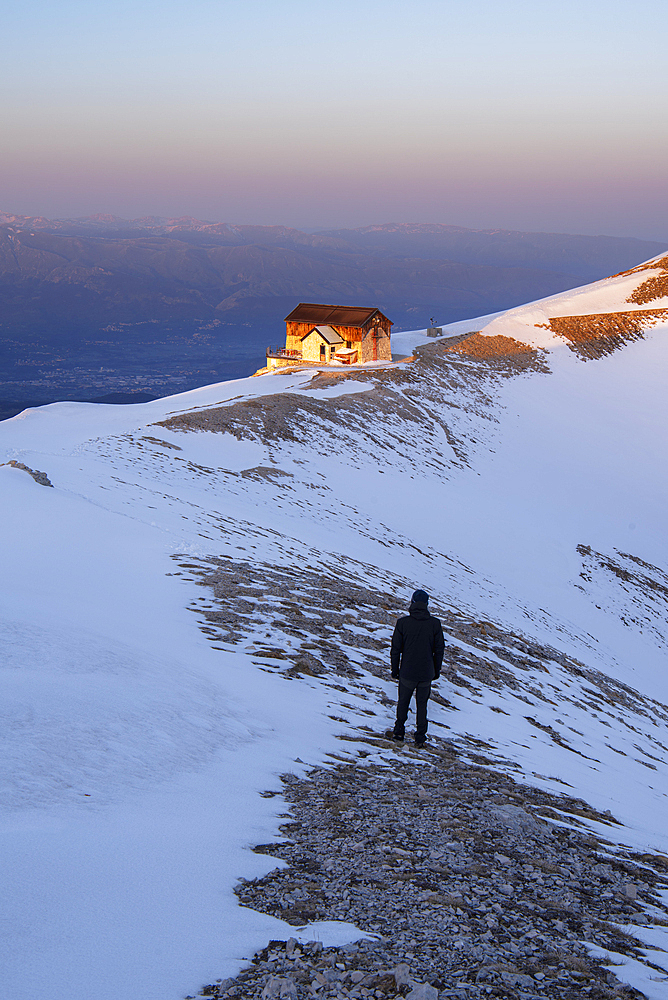 Winter view of a hiker admiring the sunset at Duca degli Abruzzi mountain hut, Campo Imperatore, Apennines, L'Aquila district, Abruzzo, Italy, Europe