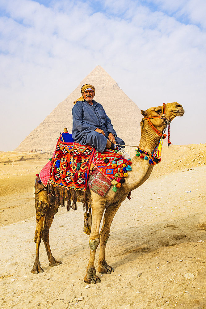 Giza, Cairo, Egypt. February 18, 2022. Man on a camel with deocrated blanket and halter at the Great Pyramid complex in Giza.