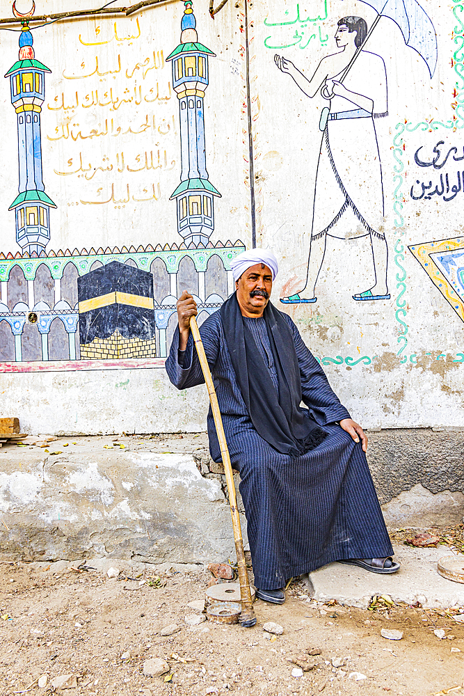 Thebes, Luxor, Egypt. February 26, 2022. Seated man in front of contemporary murals on in Luxor.