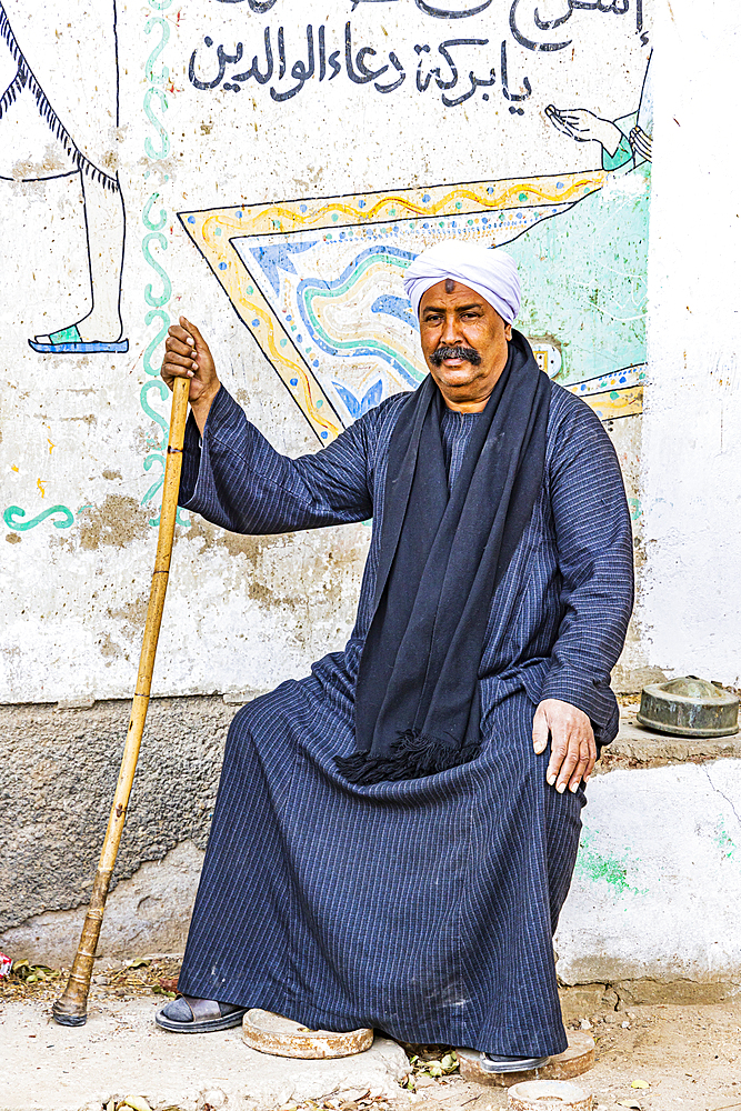 Thebes, Luxor, Egypt. February 26, 2022. Seated man in front of contemporary murals on in Luxor.