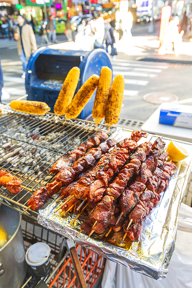 Jackson Heights, Queens, New York City, New York, USA. Meat kebabs and corn on the cob at a sidewalk food stand.