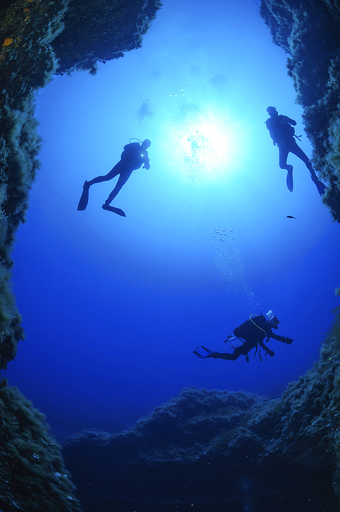 Cave exit with three divers, Grotta dei Cirri, Ustica, Italy.