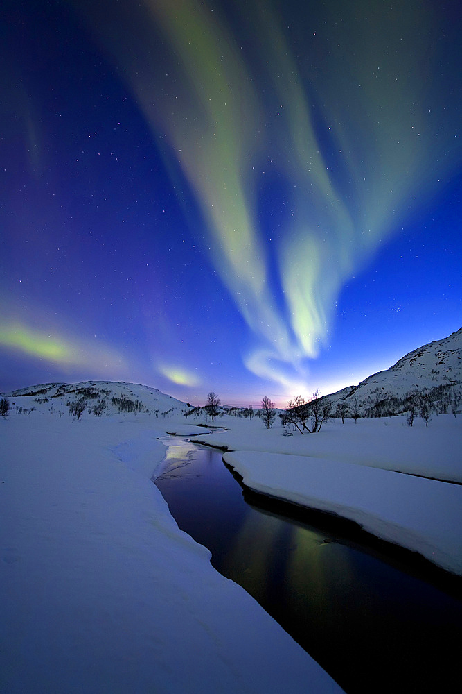 Aurora Borealis over Skittendalen Valley and the Skittendalen River in Troms County, Norway. Auroras are the result of the emissions of photons in the Earth's upper atmosphere.