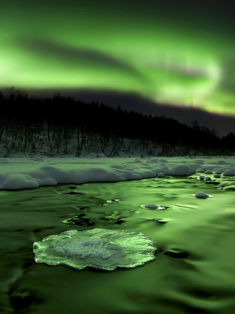 Aurora Borealis reflects off the Tennevik River, Troms County, Norway. Auroras are the result of the emissions of photons in the Earth's upper atmosphere.