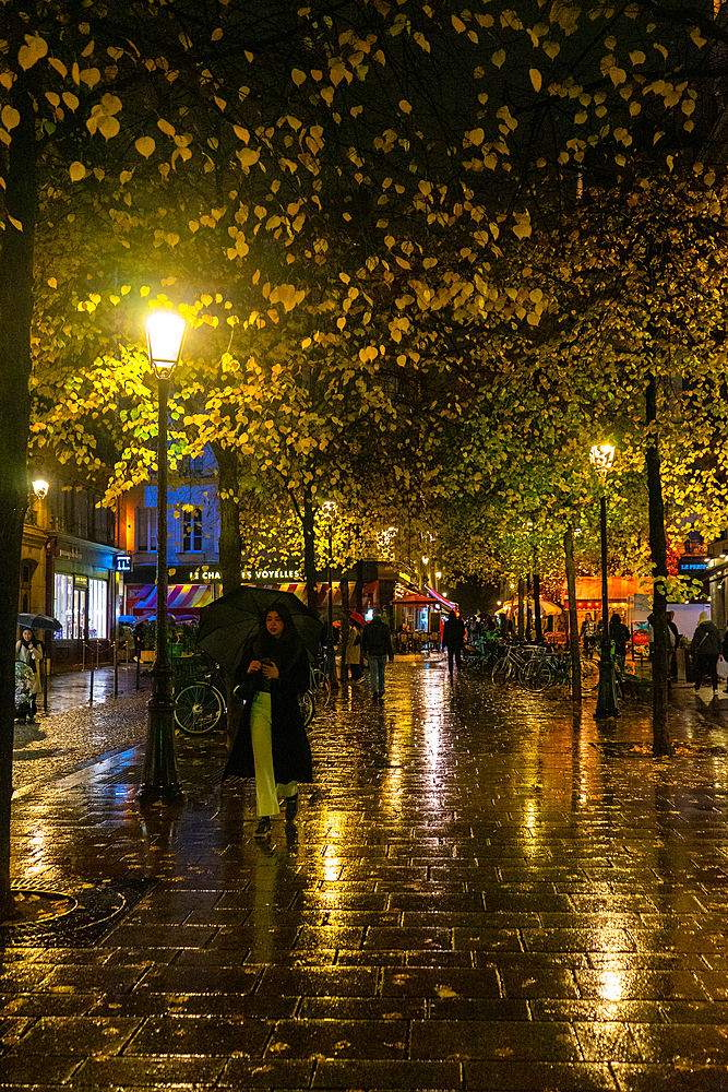 Woman holding umbrella at night in rain in Paris