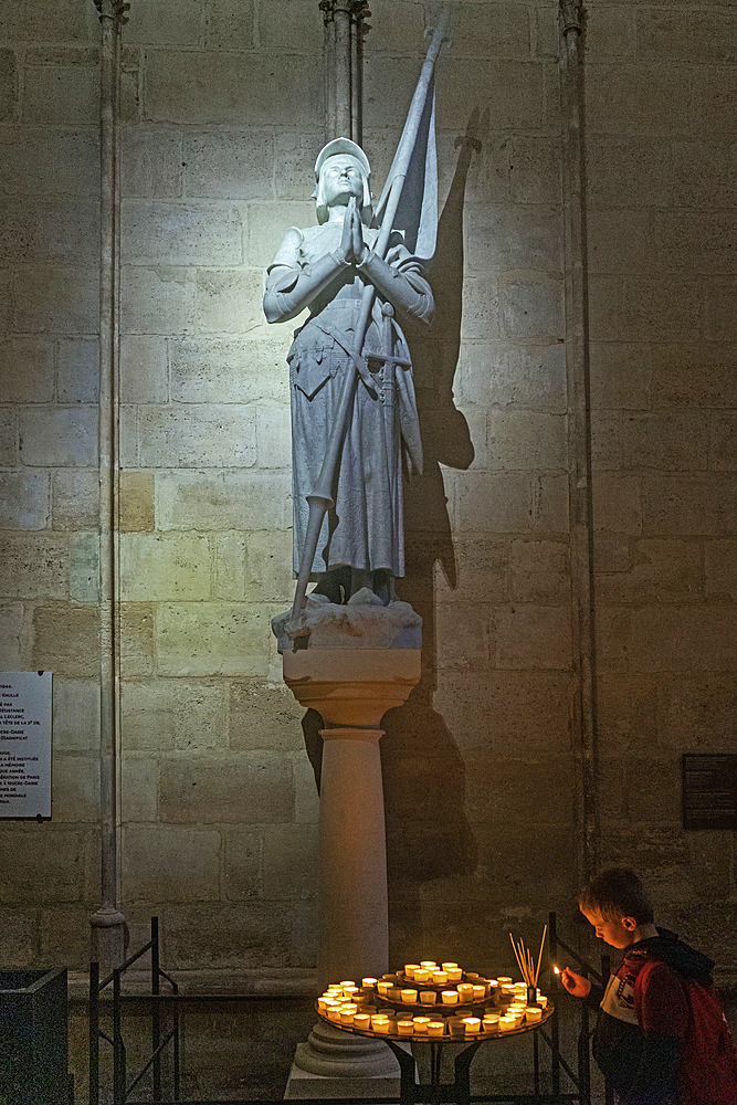 Boy lighting candle below statue of Joan of Arc in Notre Dame cathedral
