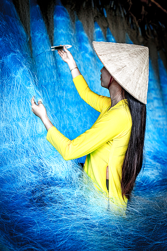 Women in a traditional ao dai mending a fishing net, Vietnam
