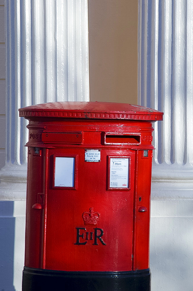 A traditional British red post box in front of cream pillars of a John Nash building near Regent's Park, London, England, United Kingdom, Europe