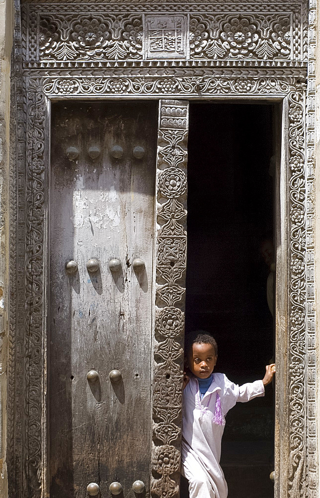 Young boy looking out from a traditional carved wooden Arab door in Stone Town, Zanzibar, Tanzania, East Africa