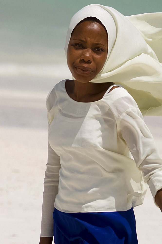 A schoolgirl walking along Kiwendwa Beach wearing a white headscarf and blue skirt, Zanzibar, Tanzania, East Africa, Africa